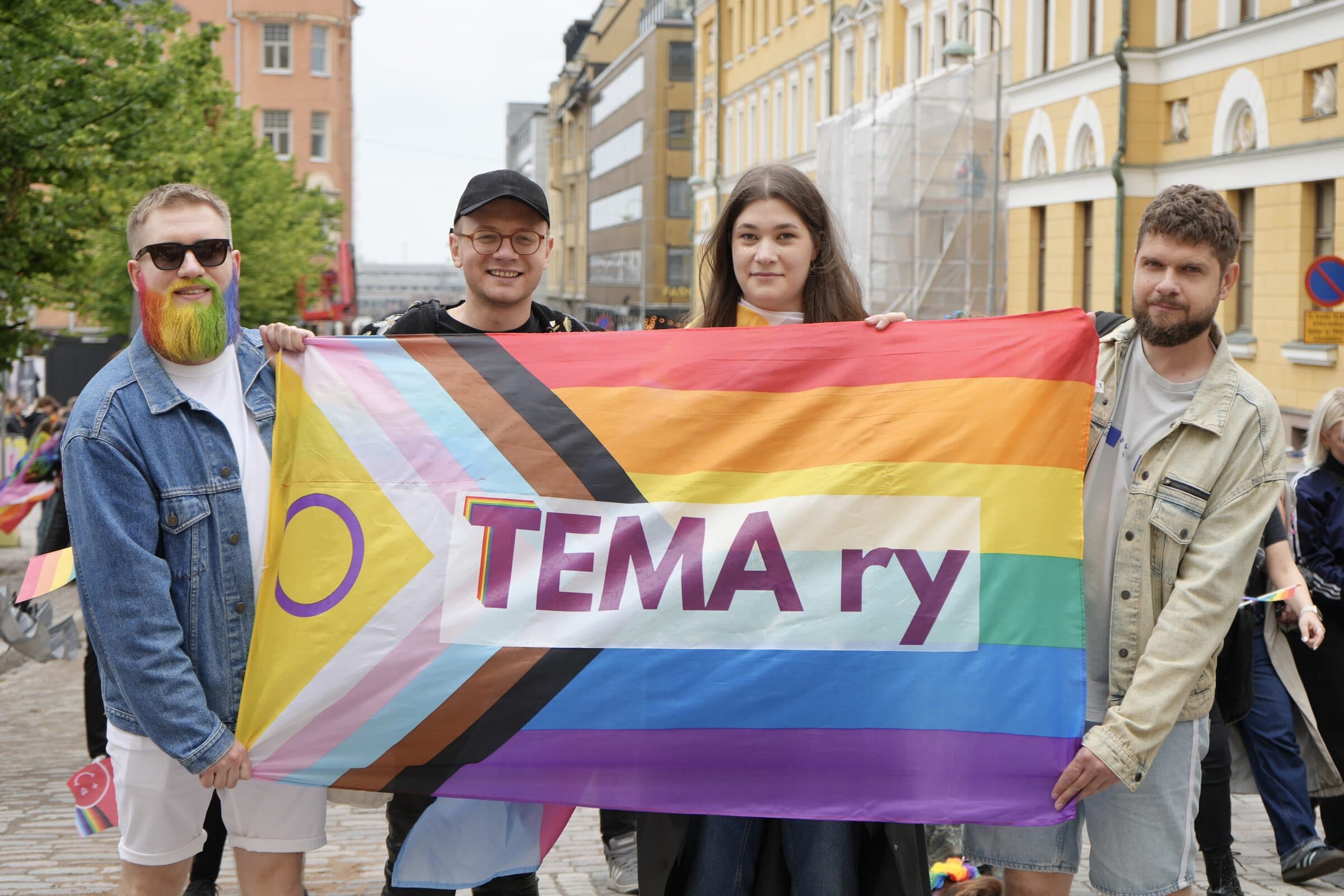 Neljä ihmistä pitelee Tema ry -lippua Helsinki Pridessa.